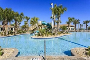 Relax by the pool surrounded by palm trees and a small bridge leading to a slide.