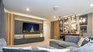 A modern living room with a large flat-screen TV, grey sofas, and a wooden entertainment unit.
