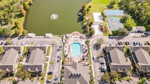 An aerial view of a residential area with a large pond, a swimming pool, and adjacent parking areas. - 4562 YR - Amazing 4 Bed Private Getaway (Kissimmee)