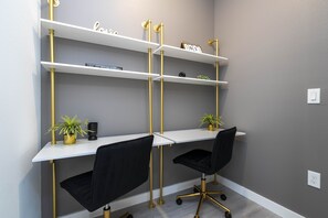 Een moderne kantoorruimte met twee bureaus, zwarte stoelen en goudkleurige schapunits tegen een grijze muur.