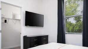 A bedroom with a bed, a TV mounted on the wall, a dresser, and a window with curtains.