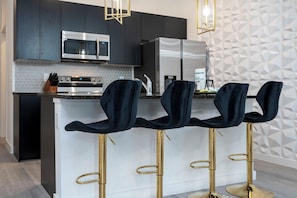 A modern kitchen with dark cabinets, stainless steel appliances, and a white island with bar stools.