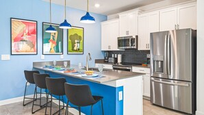 Una cocina moderna con una isla central, electrodomésticos de acero inoxidable e iluminación colgante azul.