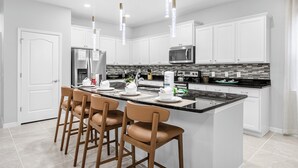 Une cuisine moderne avec des meubles blancs, un plan de travail noir et un îlot central doté de tabourets de bar.