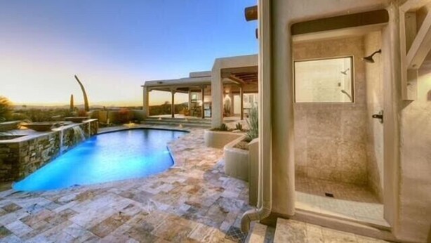 A modern outdoor pool area with a stone floor, a covered seating area, and a glass-enclosed shower. - Cimarron: Spectacular city and mountain views, pool, hot tub, and more! (Catalina Foothills)