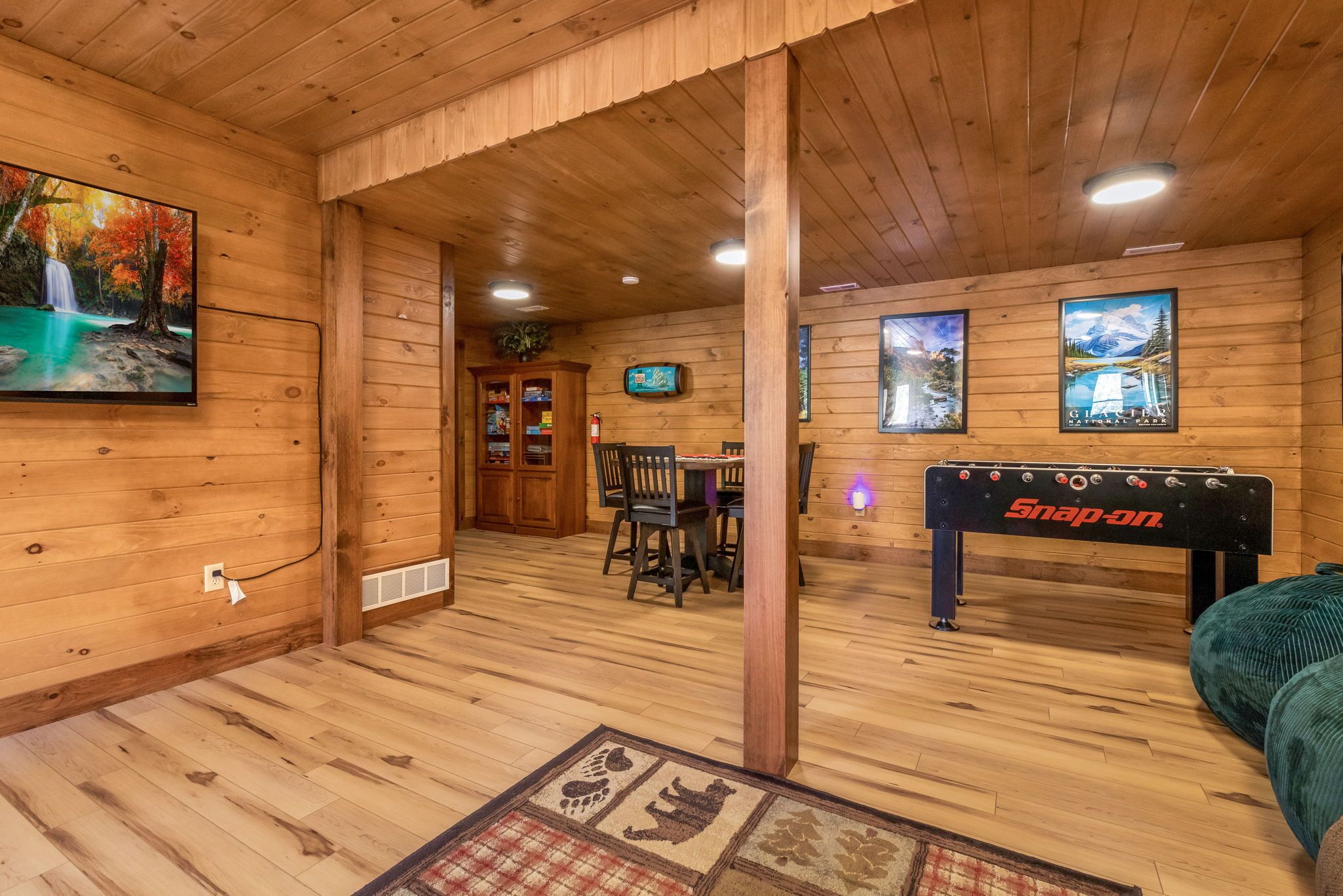 A wooden interior with a TV, a table with chairs, and a foosball table.