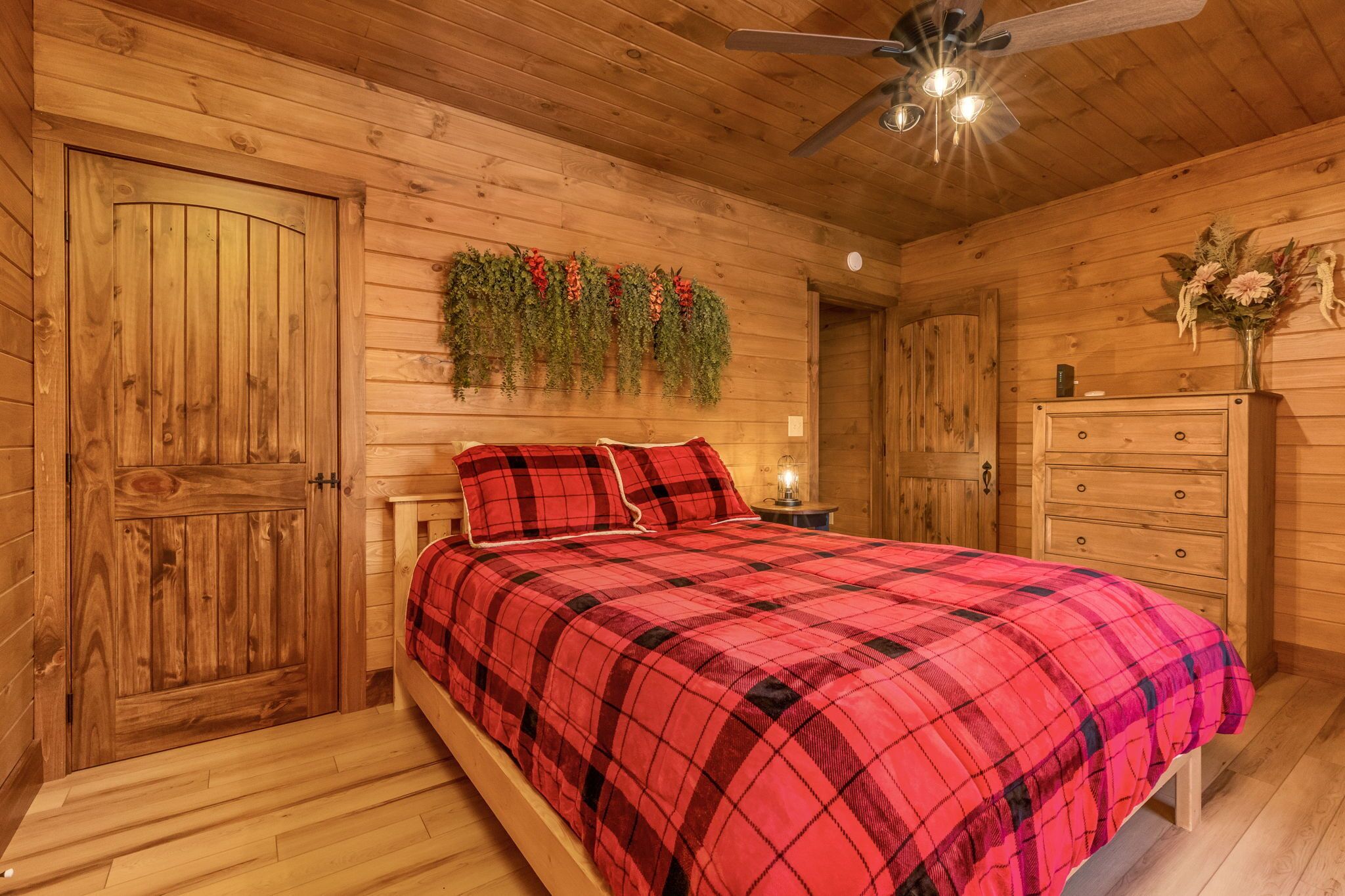 A wooden cabin bedroom with a bed, a dresser, a nightstand, and a ceiling fan.