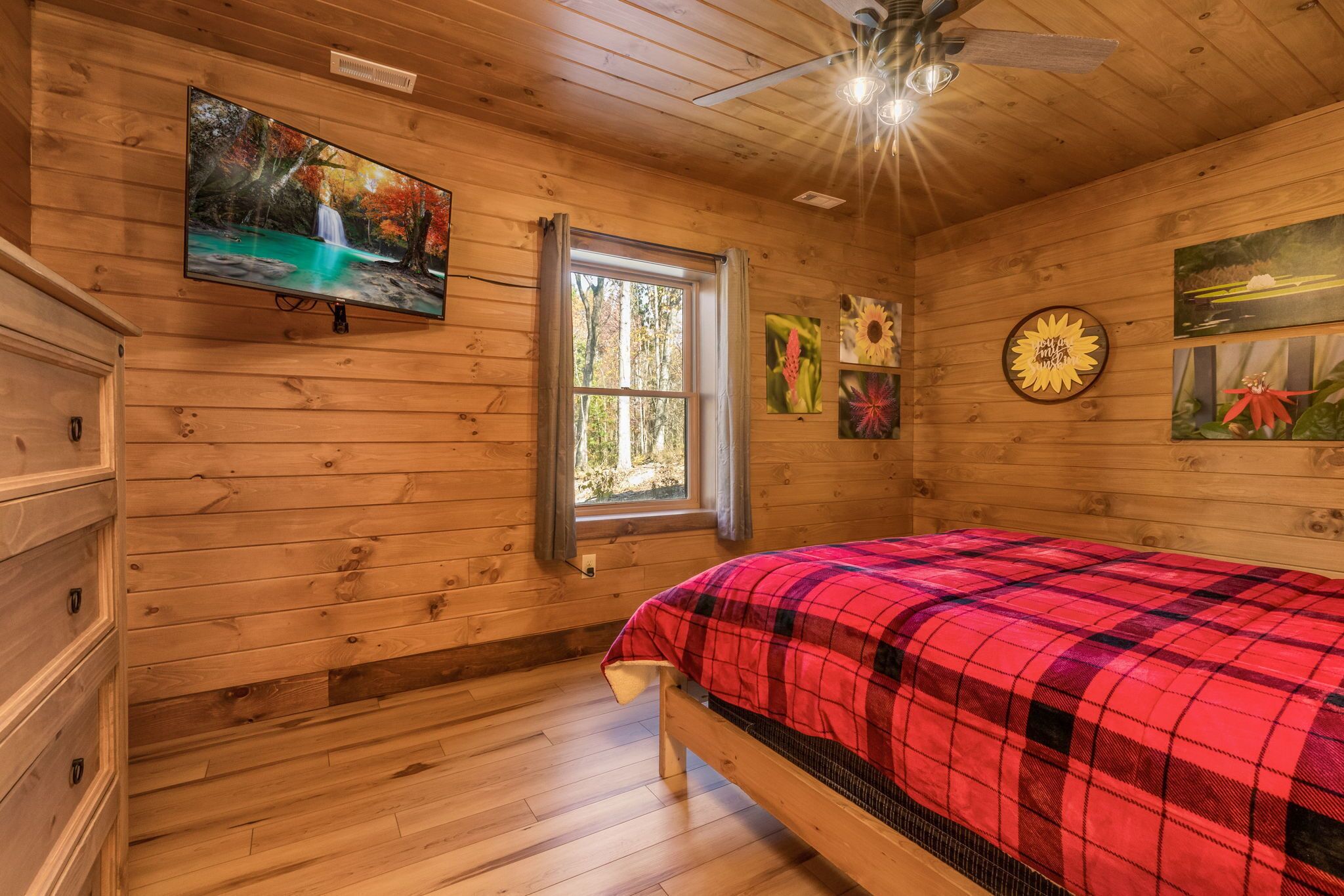 A wooden cabin bedroom with a bed, a TV, a window, and wall art.