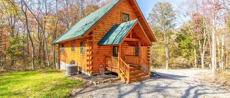 A log cabin with a green roof, a porch, and a gravel driveway.