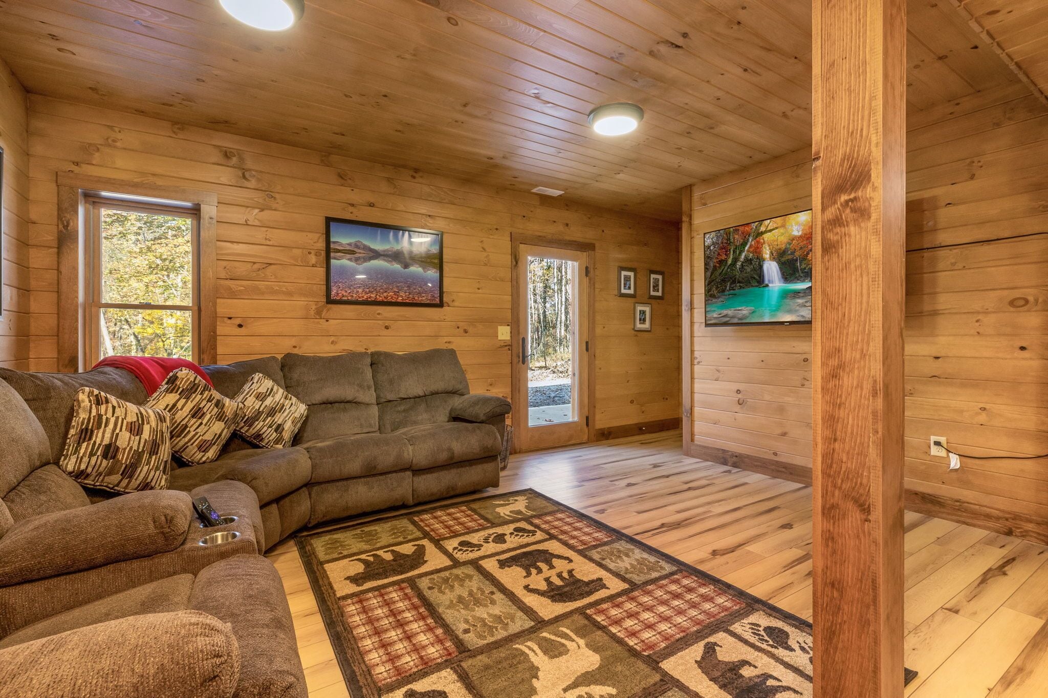 Una sala de estar acogedora con piso y paredes de madera, un sofá modular, un tapete estampado y cuadros enmarcados.