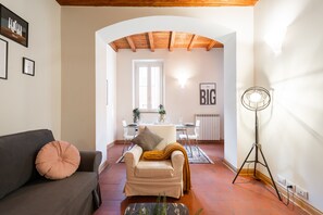A living room with a sofa, a chair, a floor lamp, and a dining area with a table and chairs. - Orso apartment (Roma)