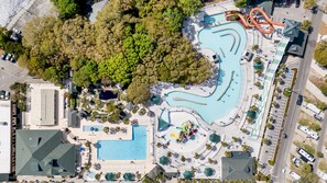 An aerial view of a resort with multiple swimming pools, a water slide, and a parking area.