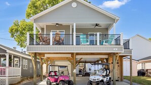 Uma casa de dois andares com garagem coberta, varanda e dois carros de golfe estacionados na frente.