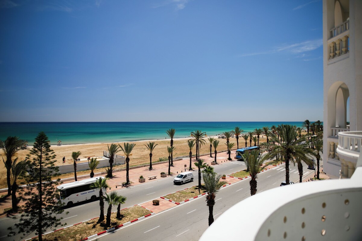 Une route côtière bordée de palmiers, un autobus et une plage en arrière-plan.