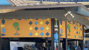 An outdoor bar area with a counter, chairs, and a wooden backdrop with palm tree decorations. - Sea Viewers Dream Oceanfront 5th floor ~ Kitchen Living room Bedroom  Pools Open (Daytona Beach)