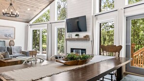 A spacious living area with a large wooden table, a fireplace, and a TV mounted on the wall. - The Cottage at Grand Marais (Grand Marais)