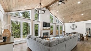 A spacious living area with a large gray sectional sofa, a fireplace, and a dining area with a wooden table and chairs. - The Cottage at Grand Marais (Grand Marais)