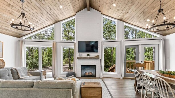 A spacious living area with a fireplace, large windows, and a wooden ceiling. - The Cottage at Grand Marais (Grand Marais)