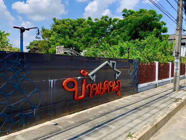 A sign with a logo and text, a fence, and trees in the background. - Baan Kenpoo Resort (Phetchaburi)