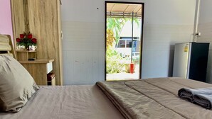 A bedroom with a bed, a wooden shelf with red roses, and a view of a house through an open door. - Baan Kenpoo Resort (Phetchaburi)