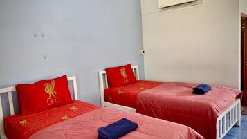 Una stanza con due letti singoli, ognuno con una coperta rossa e un cuscino con lo stemma di un leone dorato. Su un letto, un asciugamano blu.