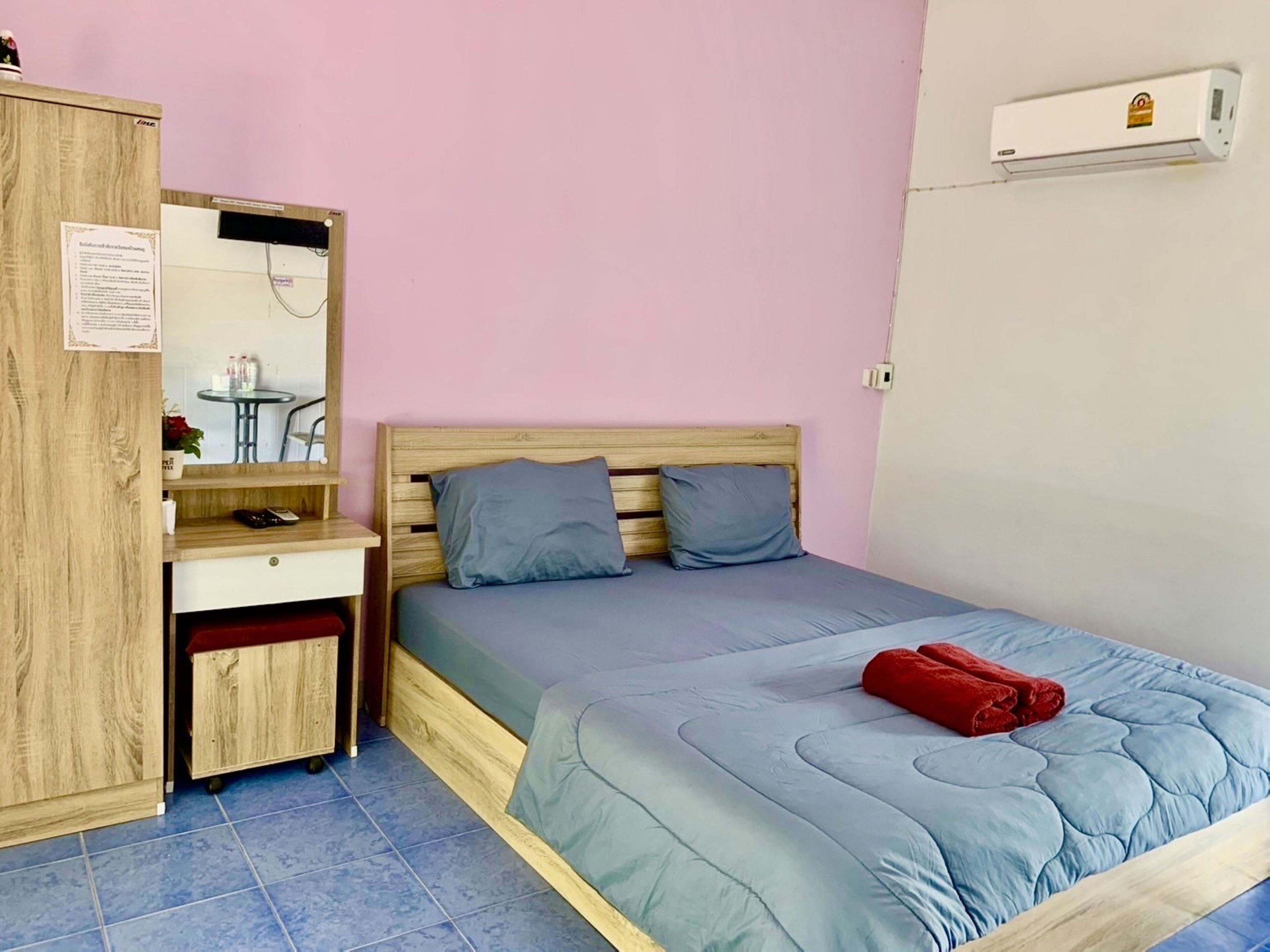 A bedroom with a bed, a wooden wardrobe, a desk with a chair, and a small table with a plant.