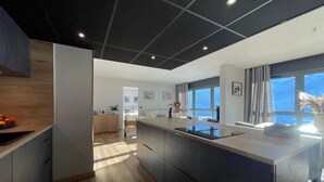 A modern kitchen with a central island, wooden flooring, and a view of the ocean through large windows. - Chez Tipère à La Mongie (Bagnères-de-Bigorre)