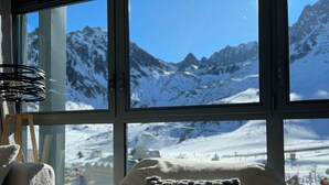 A cozy room with a large window offering a view of snow-covered mountains. - Chez Tipère à La Mongie (Bagnères-de-Bigorre)