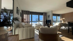 A modern living room with a large window, a sofa, a coffee table, and a dining area. - Chez Tipère à La Mongie (Bagnères-de-Bigorre)