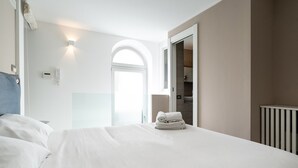 Une chambre d’hôtel avec un lit bien fait, une armoire et une salle de bain visible à travers une porte en arc de cercle.