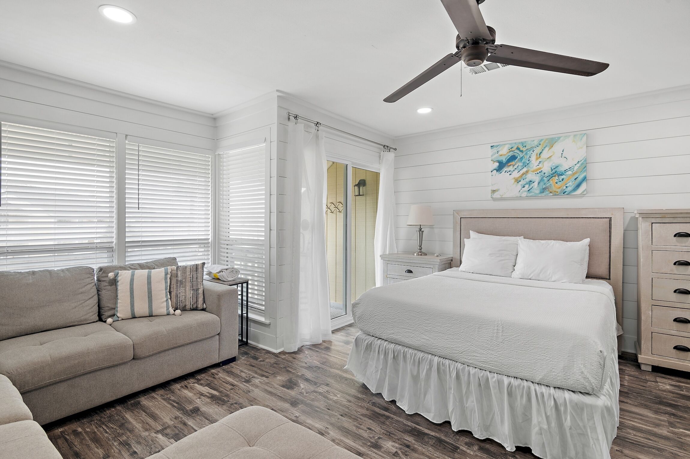 A bedroom with a bed, a nightstand, a lamp, a ceiling fan, and a window with blinds.