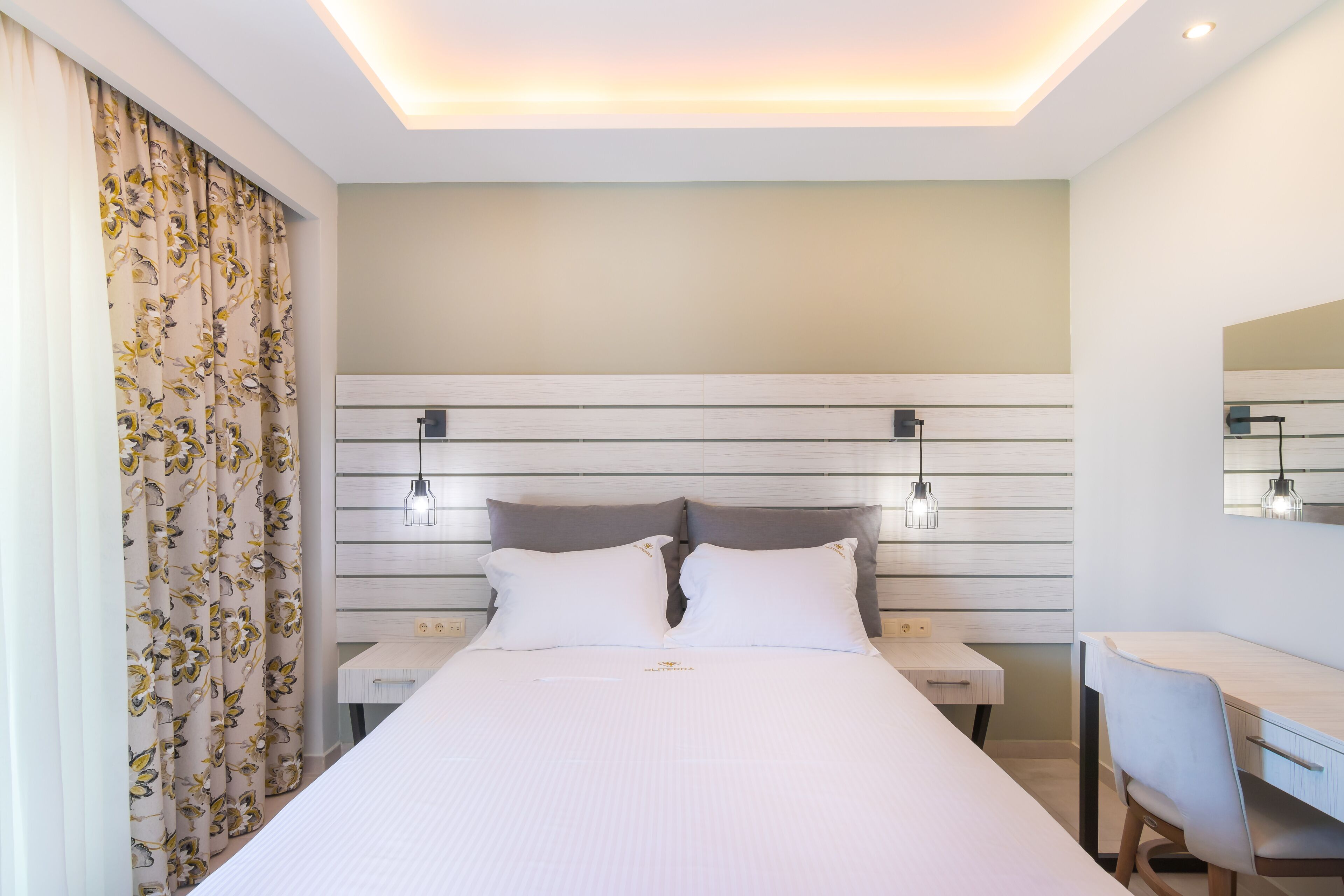 A modern hotel room with a large bed, bedside tables, a desk, and a mirror.