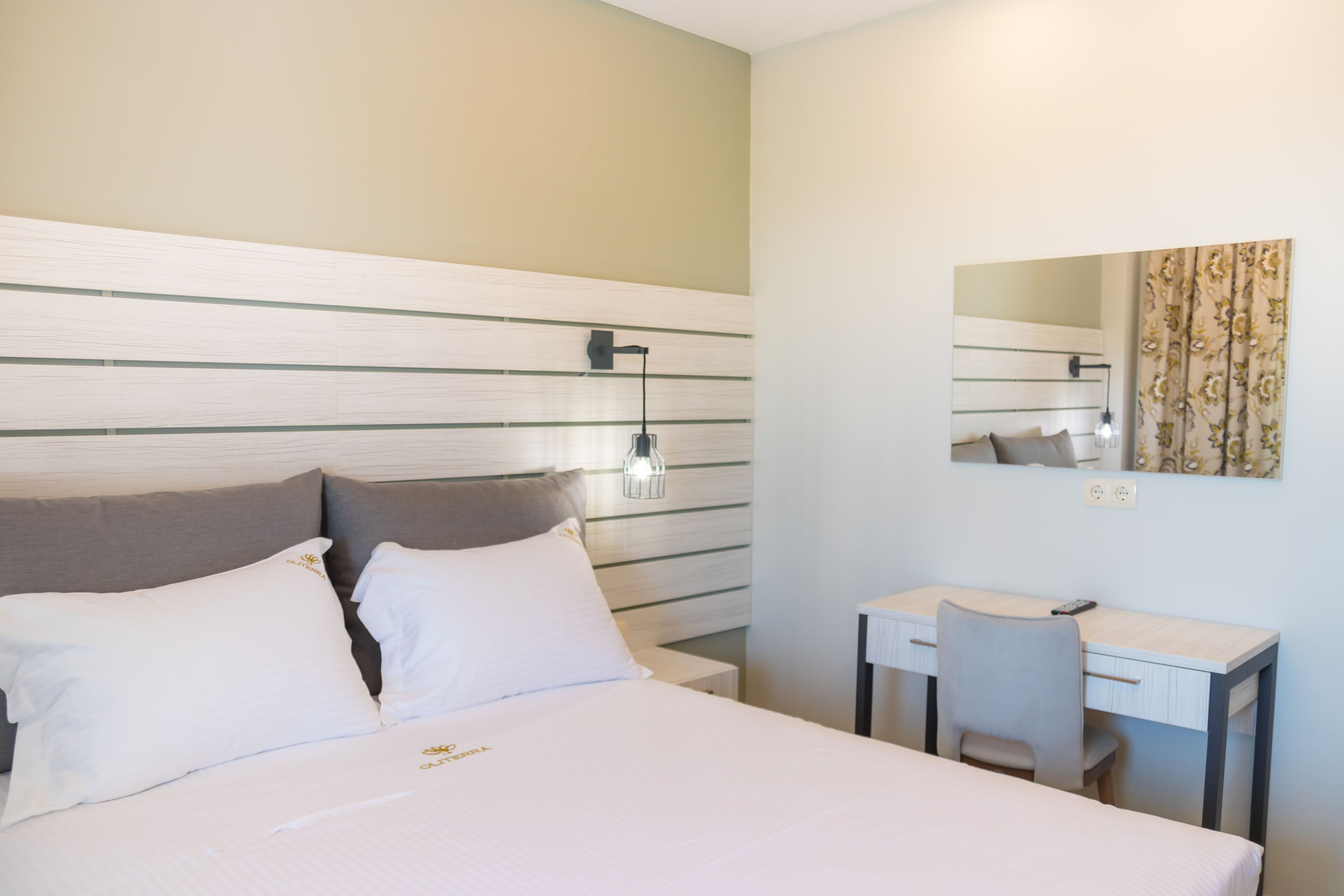 A hotel room with a bed, a desk, a chair, a lamp, and a mirror.