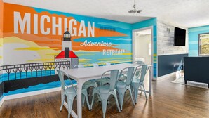 Een eetruimte met een muurschildering van de kustlijn van Michigan, een witte tafel en lichtblauwe stoelen.