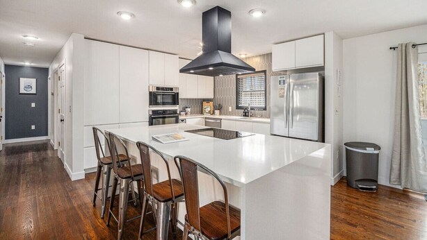 Een moderne keuken met witte kasten, roestvrijstalen apparatuur en een centraal eiland met barstoelen.