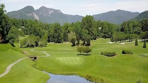 Golfkenttä, jossa on lampi, puita ja taustalla näkyviä vuoria.