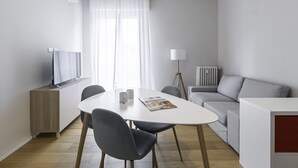 A modern, well-lit living room with a dining area, a sofa, a TV, and a lamp. - Italianway Easy - Tartini 23 (Milano)
