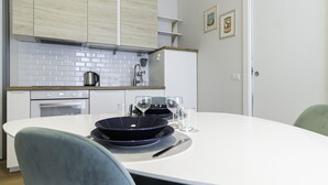 A modern kitchen with white cabinets, a tiled backsplash, and a dining table set with plates, glasses, and cutlery. - Italianway Easy - Tartini 23 (Milano)