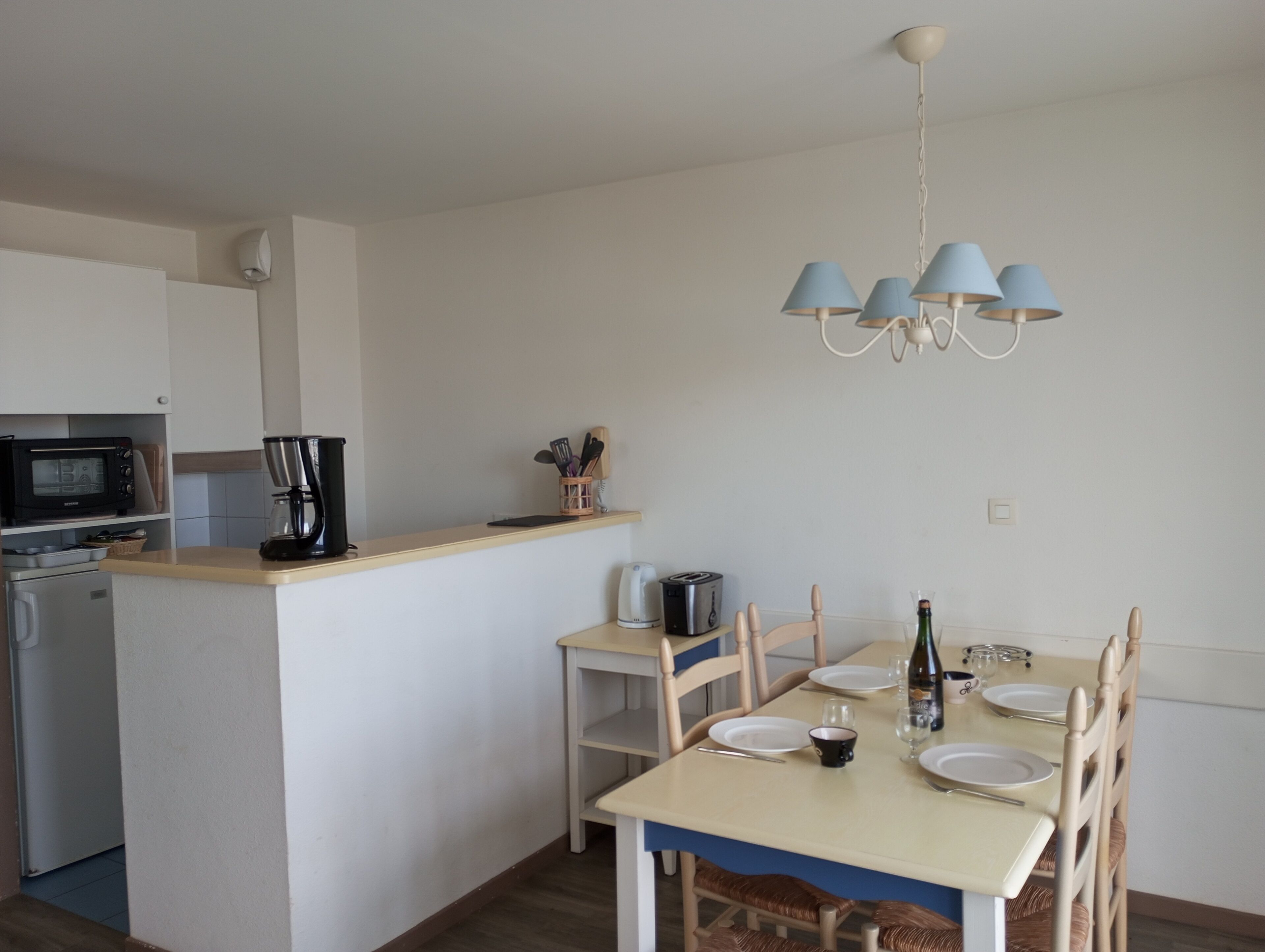 A compact kitchen with a microwave, coffee maker, and toaster. A dining table with chairs and a chandelier is also visible.