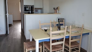 A compact kitchen with a coffee maker, toaster, and a small island with a sink. There is a dining table with chairs and a chandelier above. - Duplex vue sur le Port du Crouesty Pour 4 Personnes (Arzon)
