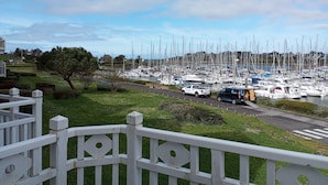 A marina with numerous boats docked, a road in the foreground, and a grassy area with a tree. - Duplex vue sur le Port du Crouesty Pour 4 Personnes (Arzon)