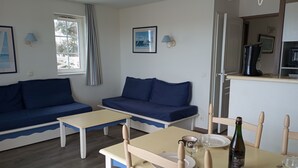 A cozy living room with two blue sofas, a small table, and a dining area with chairs and a bottle of wine. - Duplex vue sur le Port du Crouesty Pour 4 Personnes (Arzon)
