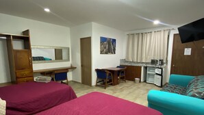 Une chambre d’hôtel avec deux lits, un bureau, une chaise, un canapé, une télévision et une fenêtre avec des rideaux.
