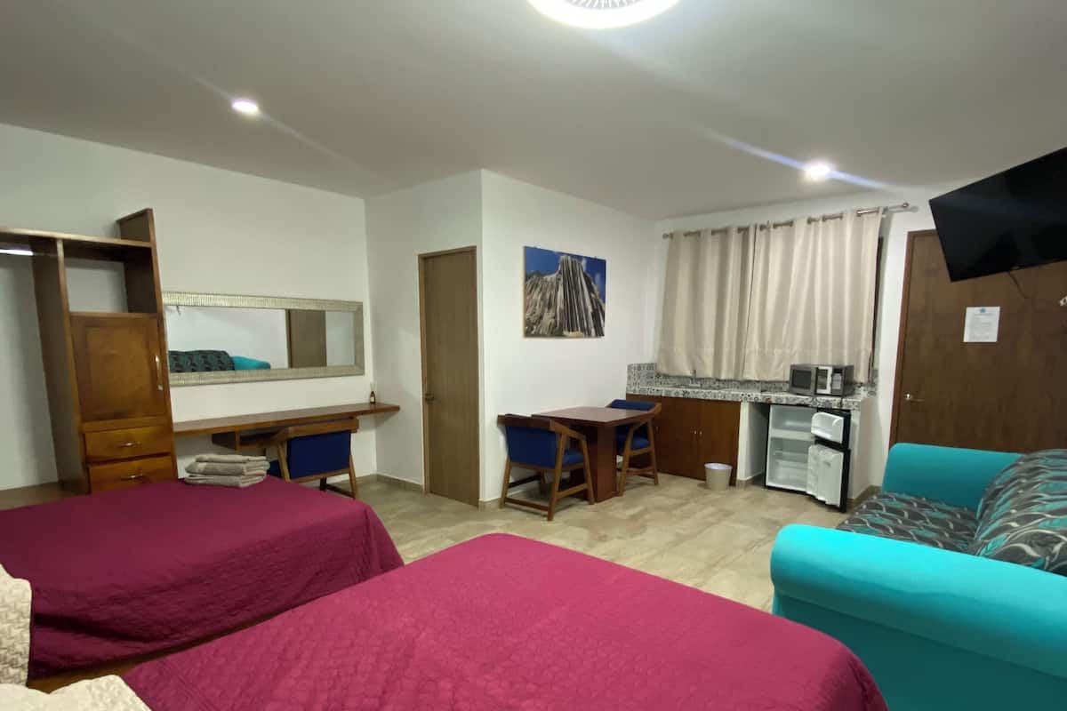 Ein Hotelzimmer mit zwei Betten, einem Schreibtisch, einem Sessel, einer Couch, einem Fernseher und einem Fenster mit Vorhängen.