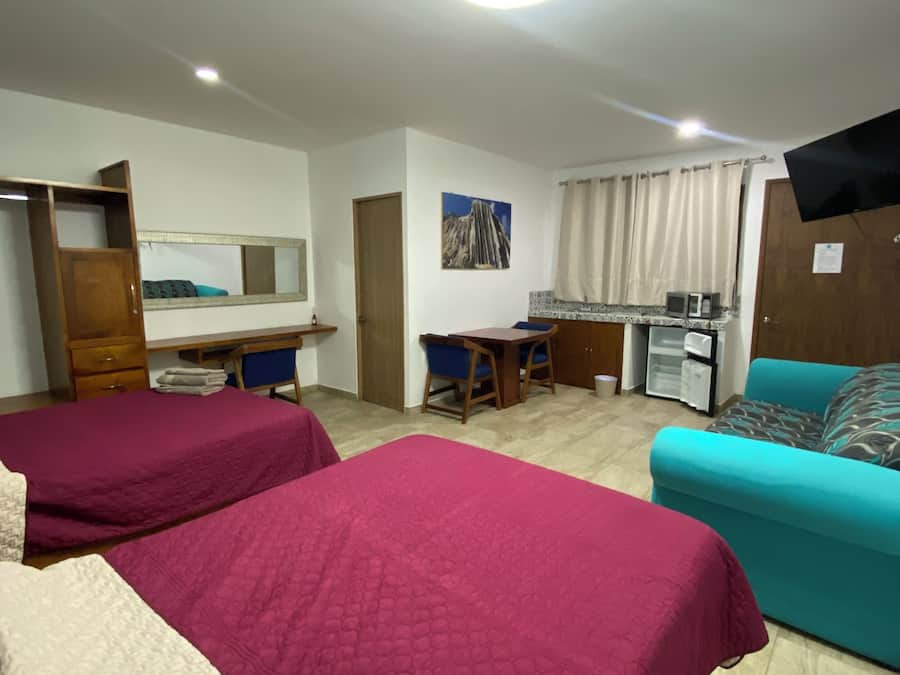 A hotel room with two beds, a desk, a chair, a sofa, a television, and a window with curtains.