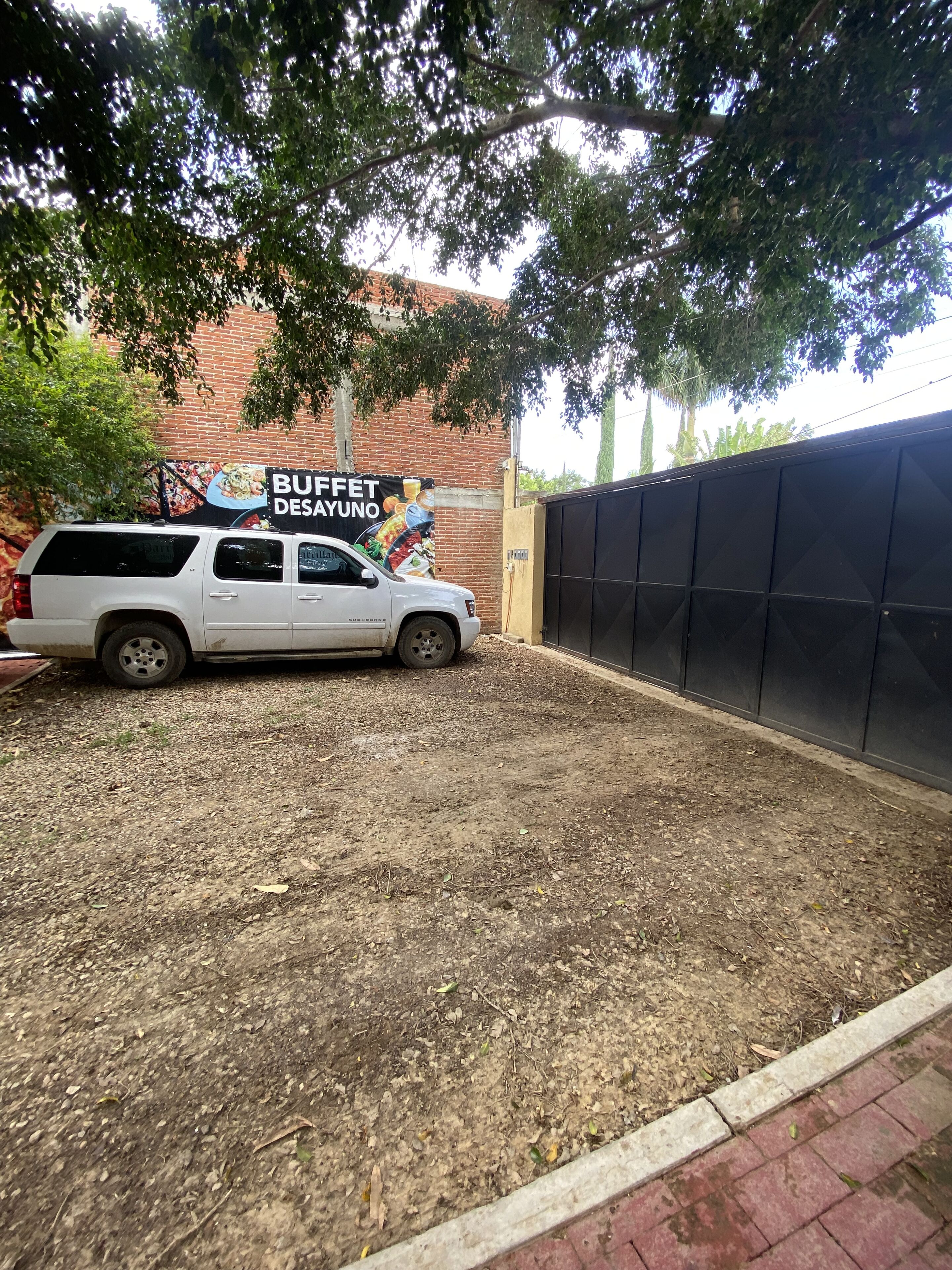 A white SUV parked in front of a brick building with a sign that reads "BUFFET DESAYUNO".