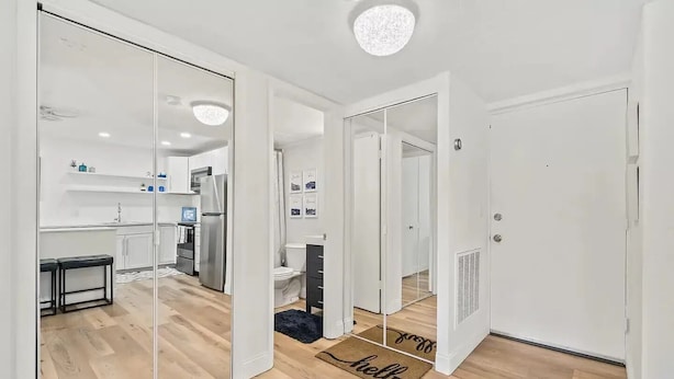 Un interior moderno con un pasillo que conduce a una cocina y un baño, destacando un espejo en la pared y un felpudo con la palabra 'hello'.