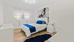 Un dormitorio moderno con cama, mesitas de noche, una ventana con cortinas translúcidas y un cuadro abstracto grande en la pared.