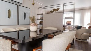 Un espace repas moderne avec une table à plateau en verre, des chaises à revêtement blanc et des œuvres d’art encadrées accrochées aux murs.