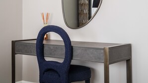 Un bureau moderne avec une chaise bleu foncé, un miroir rond et un petit objet décoratif sur le côté.